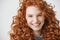 Close up of redhead beautiful girl with freckles smiling looking at camera over white background.