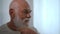 Close-up reflection in mirror of senior bearded Caucasian man combing hair smiling. Old male retiree with gray hair and