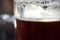 Close-Up Of Refreshing Cold Pint Of Dark Ale Beer With Condensation, Frothy Foam And Bubbles Ready To Drink