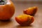 Close up of ripe fresh slices of persimmon and whole fruit on wooden background