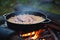 close-up of risotto cooking in cast iron pan on campfire
