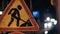 Close-up of a road sign warning drivers about road works. Grunge road traffic sign. Signal lights flash in the