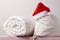 Close-up of a rolled duvet and a pillow with a cap of Santa Claus lying on the chest, on the background light walls