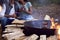 Close Up Of Romantic Couple Camping Sitting By Bonfire In Fire Bowl With Hot Drinks