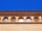 Close up of the roof line of an old stone spanish building with curved tiles and ornate windows with a bright blue sunlit sky