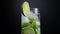 Close-up of a rotating misted glass of mojito with lime slices, mint leaves and ice cubes