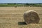 Close-up of a round haystack in the foreground with other ones dispersed in a field in the French countryside with vineyards in th