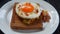 Close-up of a round shaped roasted egg with raw vegetables on a whole grain bread on a white plate. Appetizer. Snack