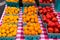 Close-up of rows of blue quart containers of small red and yellow tomatoes on a white and red checkered tablecloth