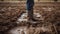 Close up of rubber boots in muddy field. Farmer inspects property after heavy rain and flooding