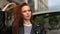 Close-up of sad attractive redhead young woman touching wet hair after autumn rain in city street.