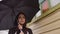 Close up of sad woman with umbrella standing near house. Portrait of thoughtful female looking away and standing on