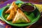 Close-up of samosas with a side of tamarind sauce on a vibrant green plate, ready to be savored