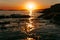 Close up of the sea through the rocks in the coast with a massive orange sunset over the islands as the background