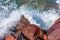 Close up of sea water breaking over reddish brown rocks forming foam, rocky coastal shoreline