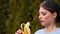 Close-up seductive attractive young woman with dark hair and red lips in blue jacket peeling banana and biting it