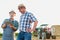 Close up of senior farmer using digital tablet with mature farmer standing against tractor in field