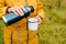 Close-up of senior woman\\\'s hand holding thermos and iron mug, pouring hot tea outdoors.