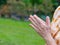 Close-up of senior woman`s hands joined together for praying while standing in a garden. Focus on hands wrinkled skin