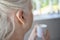 Close Up Of Senior Woman Wearing Behind The Ear Hearing Device Or Aid With Hot Drink At Home