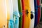 Close up Set of different color surf boards with fins in a stack on sandy beach for rent. Multicolored surfboards as