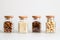 Close up. Set of kitchen glass jars. Inside contain raisins, sesame, hazelnuts, almond. White background. Copy space