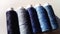Close-up of several bobbins and spools of thread in different shades of blue. A white background