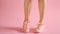 Close up of shapely female legs walking in sneakers on coral background