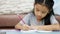 Close up shot Asian little girl using pencil write to a note book doing homework with concentration for home school and education