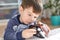 Close up shot of attractive brunet male kid plays with his favourite toy car, tries to repair wheel, has concentrated look, spends