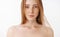 Close-up shot of attractive feminine naked redhead woman with freckles posing over gray background sensualy with