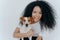 Close up shot of beautiful happy Afro woman with bushy curly hair, embraces favourite dog and have fun together at home, expresses