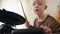 Close-up shot from below of a happy blond albino boy with white hair setting up an electronic drum kit before starting