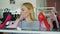 Close-up shot of blond young woman choosing high-heel shoes in footwear store. She is examining different heels