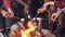 Close-up shot of burning campfire and people`s hands holding sticks with marshmallow above flame and tourists` legs