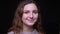 Close-up shot of cute young brunette wavy-haired student smiling with satisfaction into camera at black background.