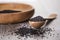 Close up shot of dried seeds of black cumin seeds kalinji on wooden spoon with wooden plate on background. Soft focus