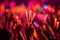 A close-up shot of hands holding glow sticks in the air at a rave party with a blurry crowd of people dancing in the background.