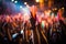 A close-up shot of hands holding glow sticks in the air at a rave party with a blurry crowd of people dancing in the background.