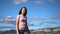 Close up shot of happy attractive girl or young woman in pink shirt and blue ripped jeans, walking along the sea on