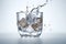 A close-up shot of ice cubes falling into a glass of clear liquid, captured from the top-down angle, with a white background that