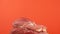 Close-up shot of a large butcher knife cutting into a fresh piece of red meat on a bright orange background. Butcher shop theme. C