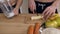 Close up shot of male hands slicing banana and female hands mixing milk in the mixer in the kitchen.