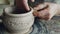 Close-up shot of muddy male potter`s hands shaping and fixing ears of ceramic bowl. Nimble craftsman is forming clay