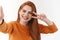 Close-up shot positive good-looking redhead woman with ginger long hair, holding camera with extended arm, showing peace