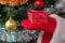 Close up shot of Santa Claus holding a red gift box in one hand. Christmas tree with red, white, and golden balls, white tinsel