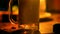 Close-up shot, someone is pouring a sparkling soda drink into a glass on a table with warm candle light at lounge bar.