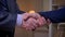 Close-up shot of two senior businessmen shake hands on the bookshelves background.