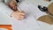 Close-up shot of woman`s hand drawing outlines of stylish ladies` garment. Paper, tailor`s scissors, ruler and coffee