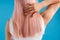 Close up shot of woman touching her smooth sleek natural long pink dyed hair while posing isolated over blue studio